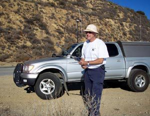 Picture of a gentleman t-hunting with an antenna and a silver truck in the background.